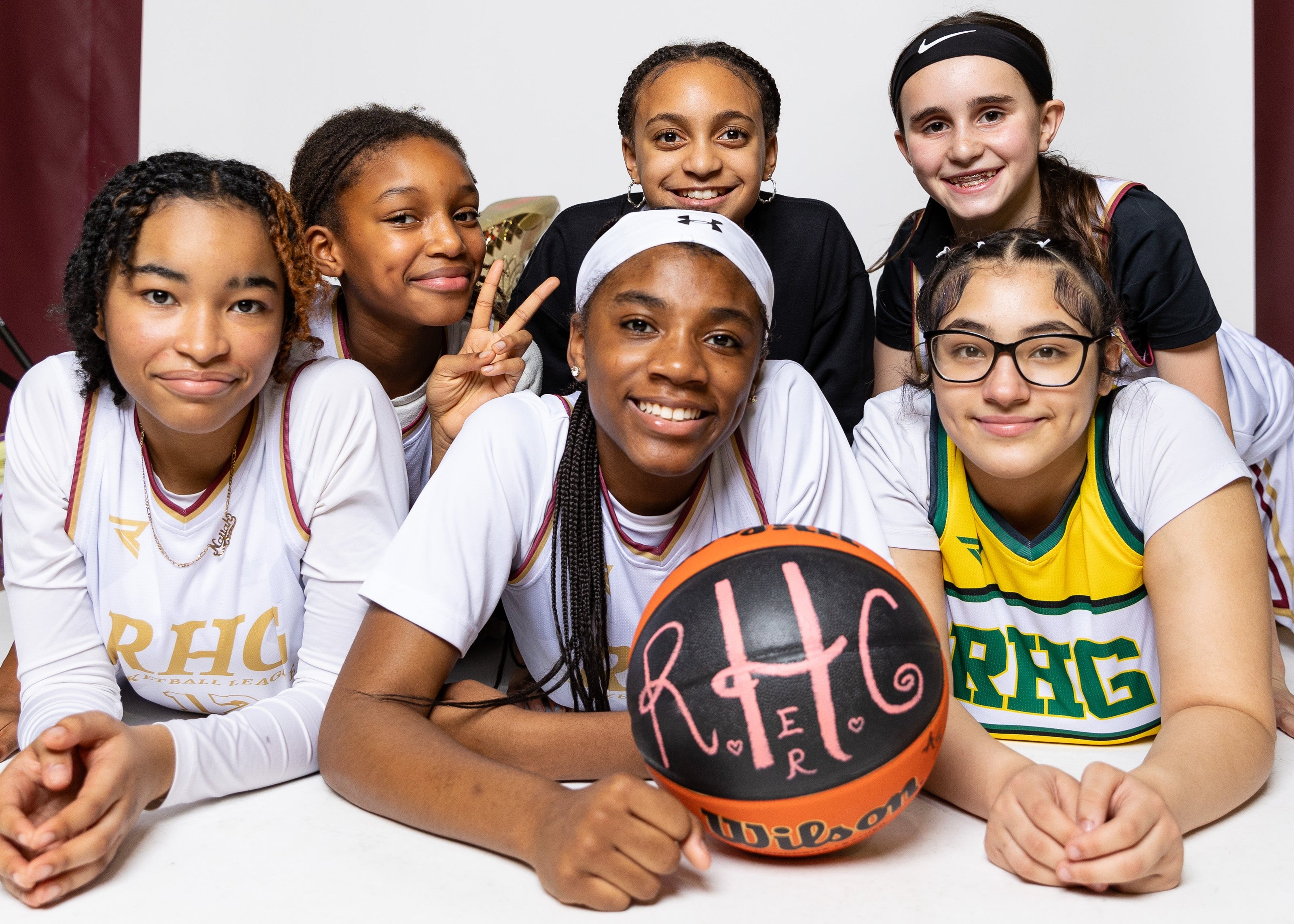Group of young girls posing with a basketball, wearing sports jerseys, in a studio setting.